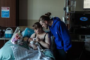 Medical staff attend to a patient in a hospital room with monitoring equipment and blue curtains visible.