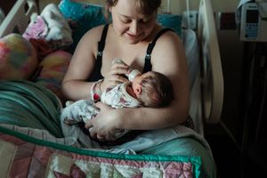A newborn baby rests peacefully in a hospital room bed surrounded by colorful blankets and medical equipment.