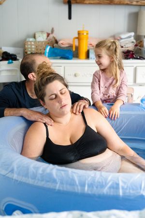 A pregnant woman rests comfortably on a blue birthing ball during labor while receiving support and massage.