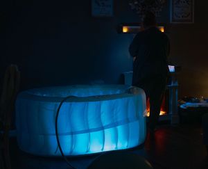 An inflatable hot tub glows with blue LED lighting in a dark room creating a relaxing ambiance.