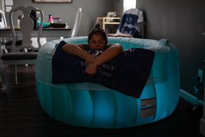 Person relaxing in a glowing aqua-colored birth pool inside a dimly lit room.