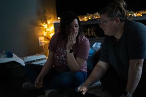 Two people sit together in a dark room illuminated by soft glowing lights in the background.
