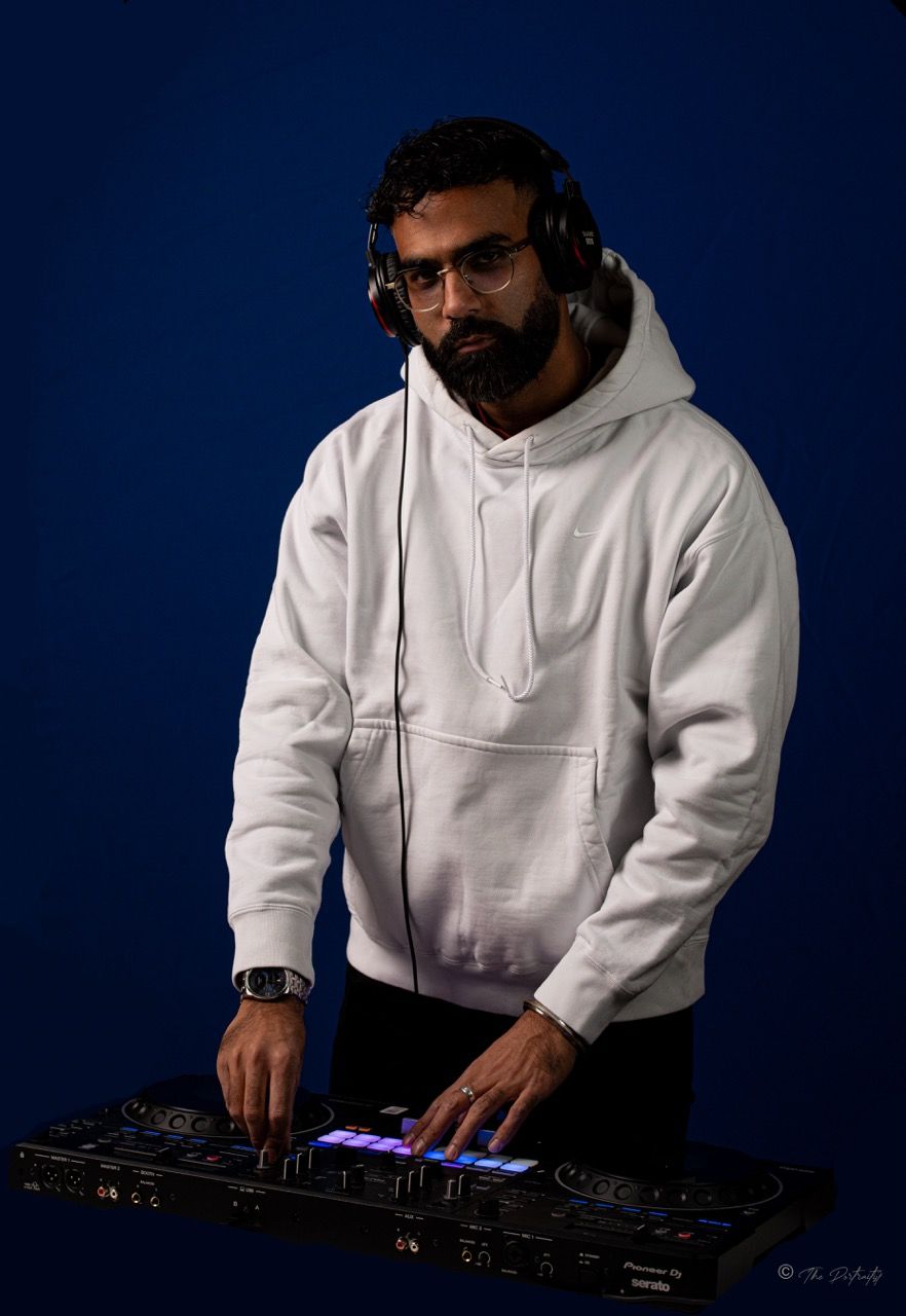 Bearded man in white hoodie using Pioneer DJ controller against blue background.