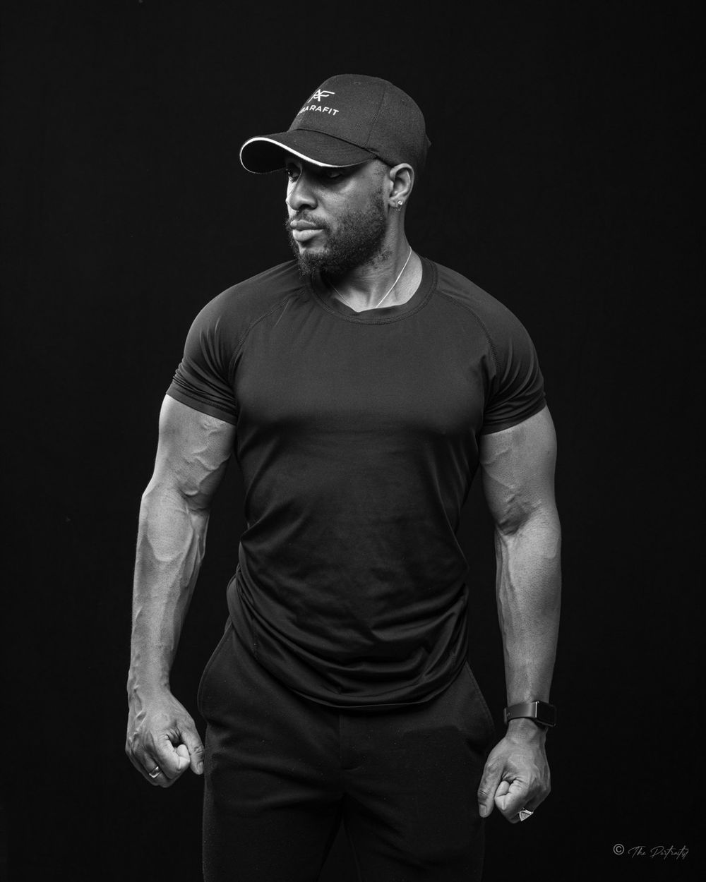 Athletic muscular man in black t-shirt and cap with clenched fists in black and white studio photo.