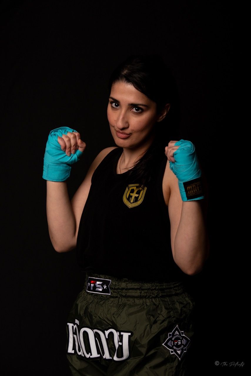 Woman in boxing gear with teal hand wraps in fighting stance wearing black tank top and green shorts.