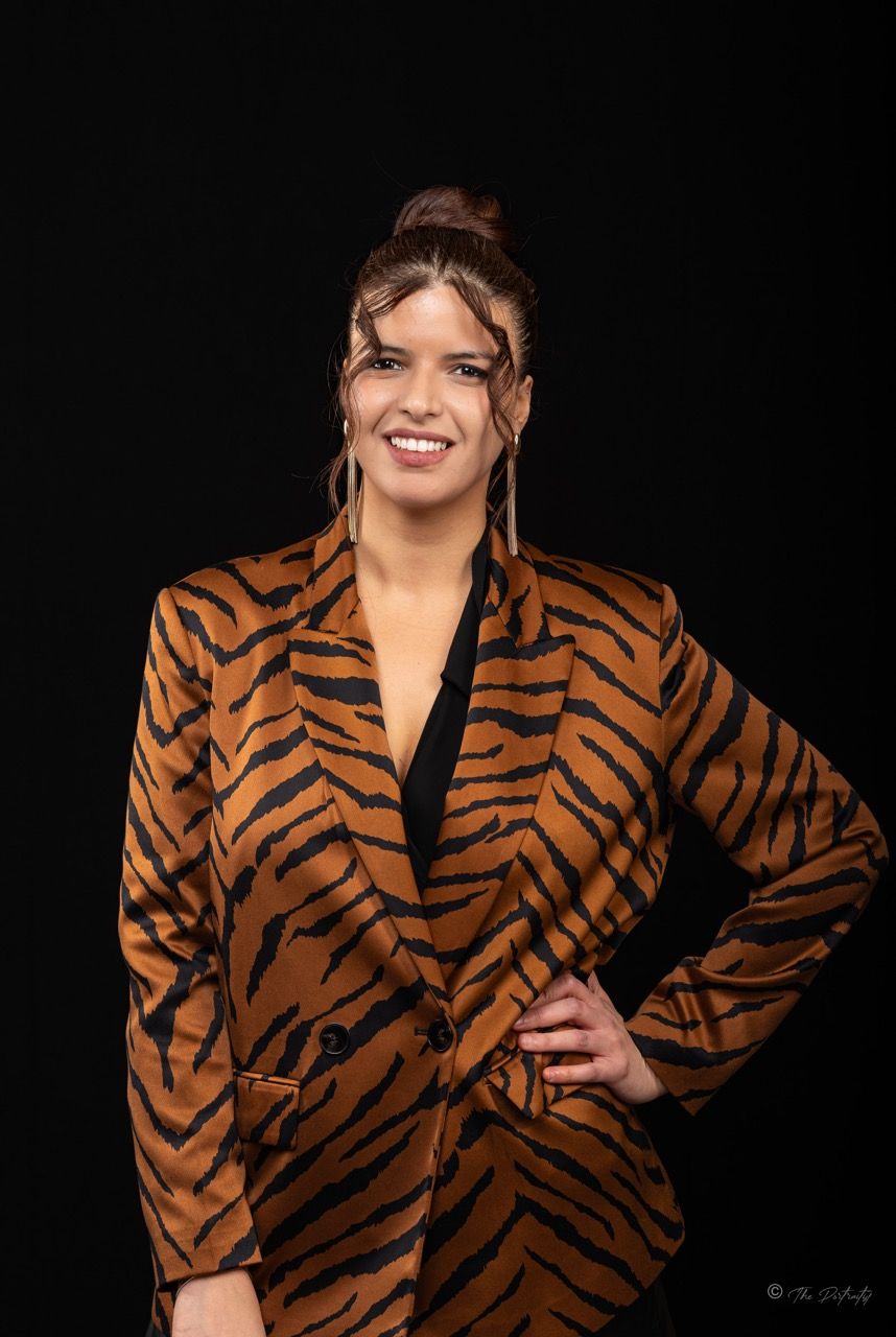 Woman smiling in tiger print blazer with hair up posing confidently against black background.