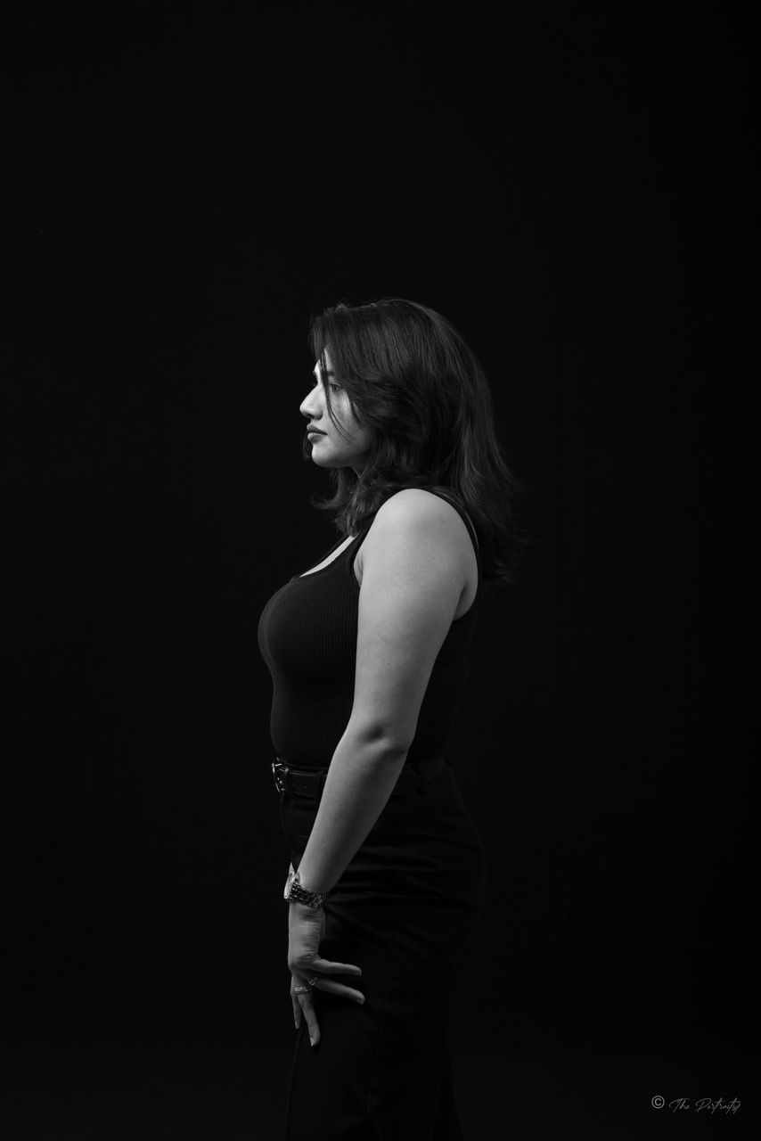 Black and white profile portrait of woman in black sleeveless top posing against dark background.