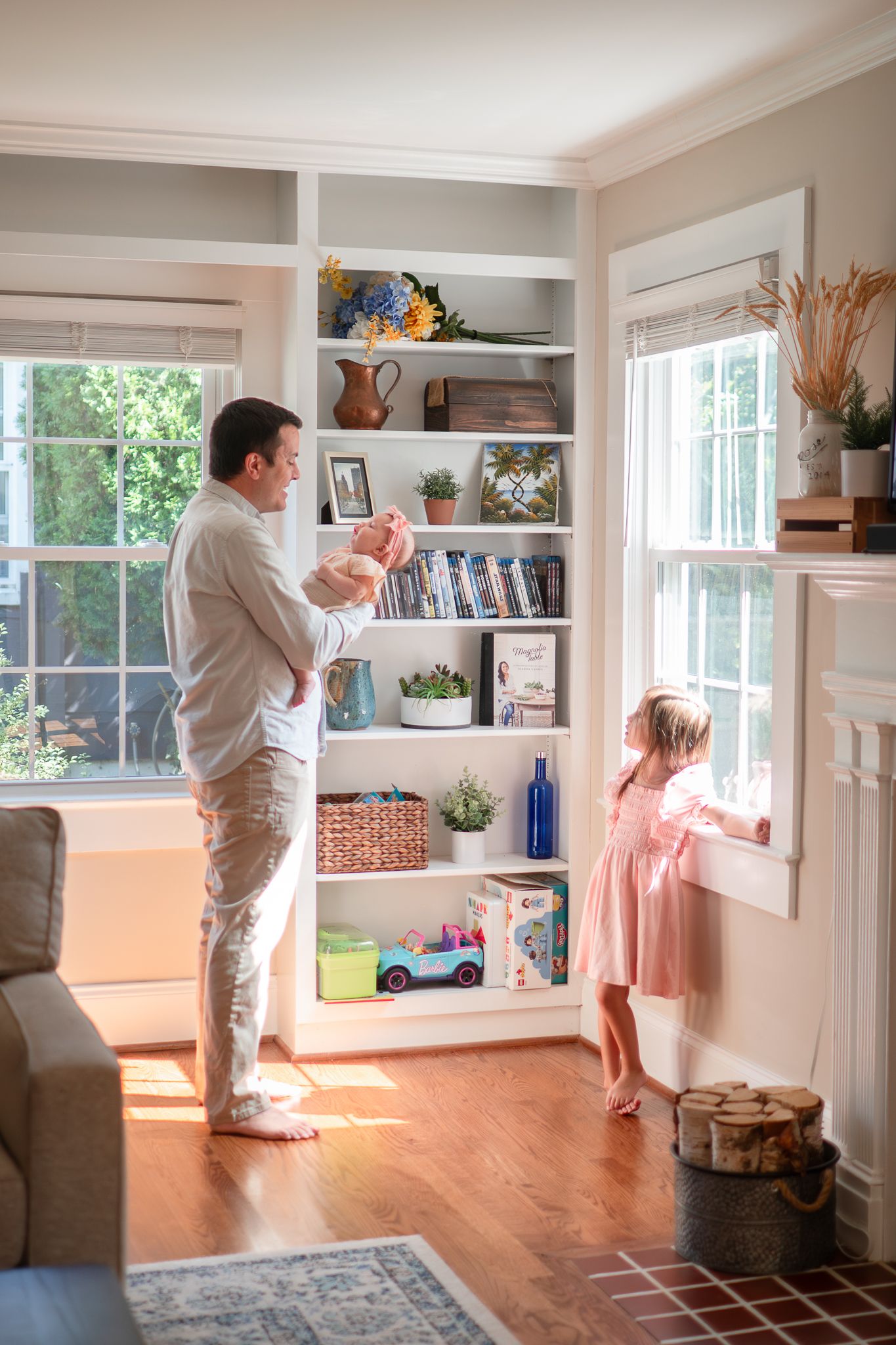 Two people dance playfully in a bright sunlit living room with hardwood floors and large windows.