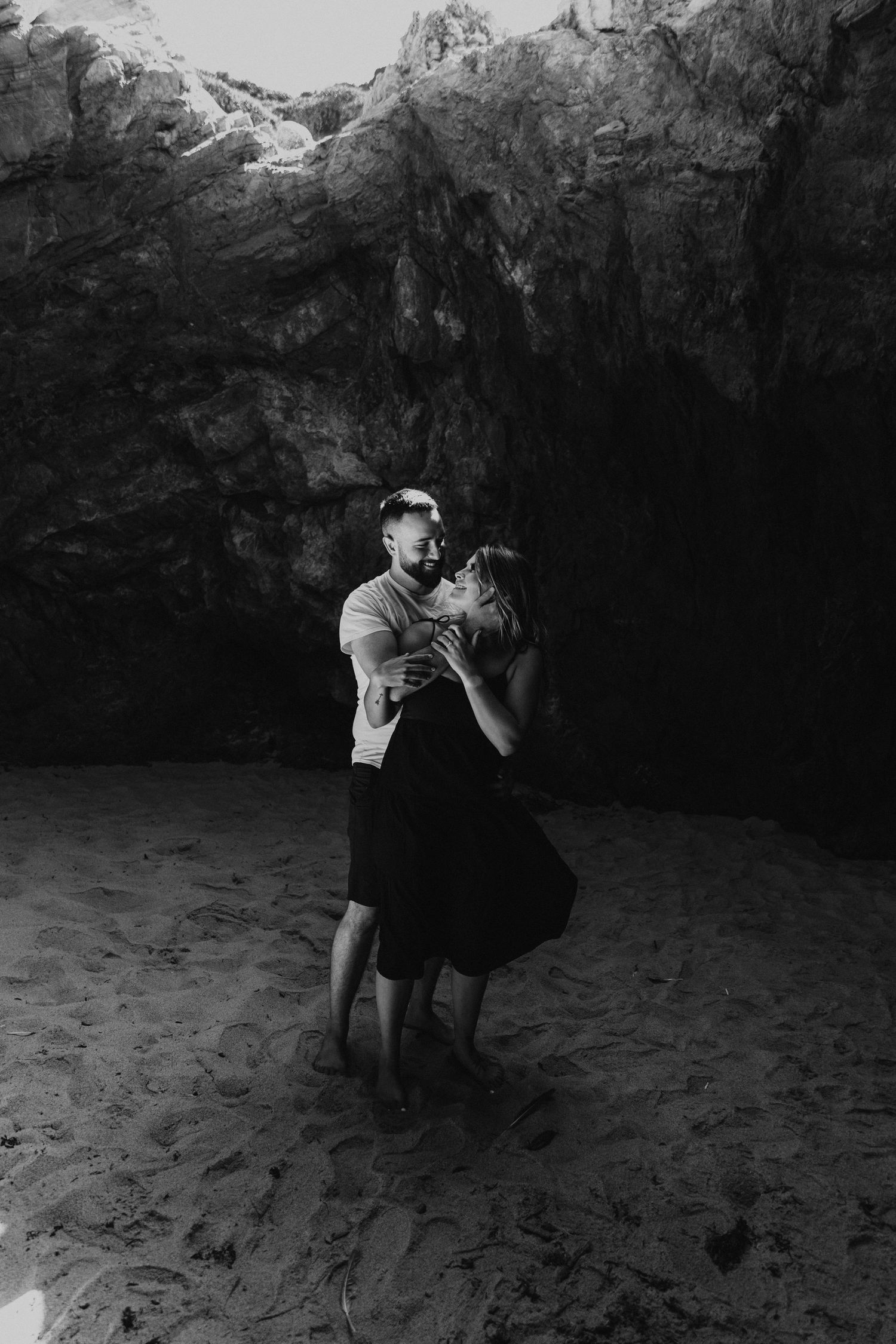 A couple poses for dramatic black and white photos in a rocky cave setting.
