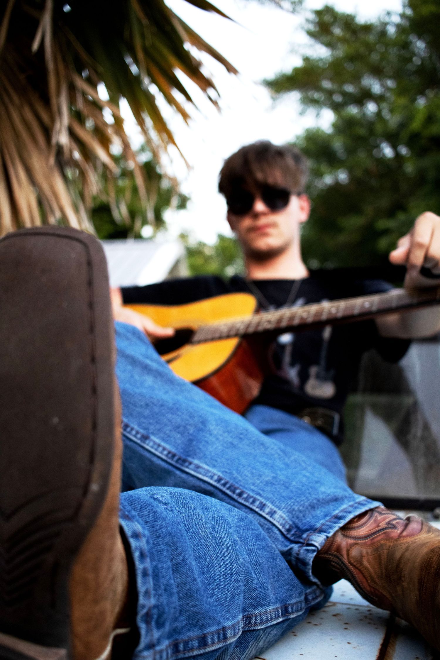 Close-up of denim jeans and boots while playing guitar on truck hood.