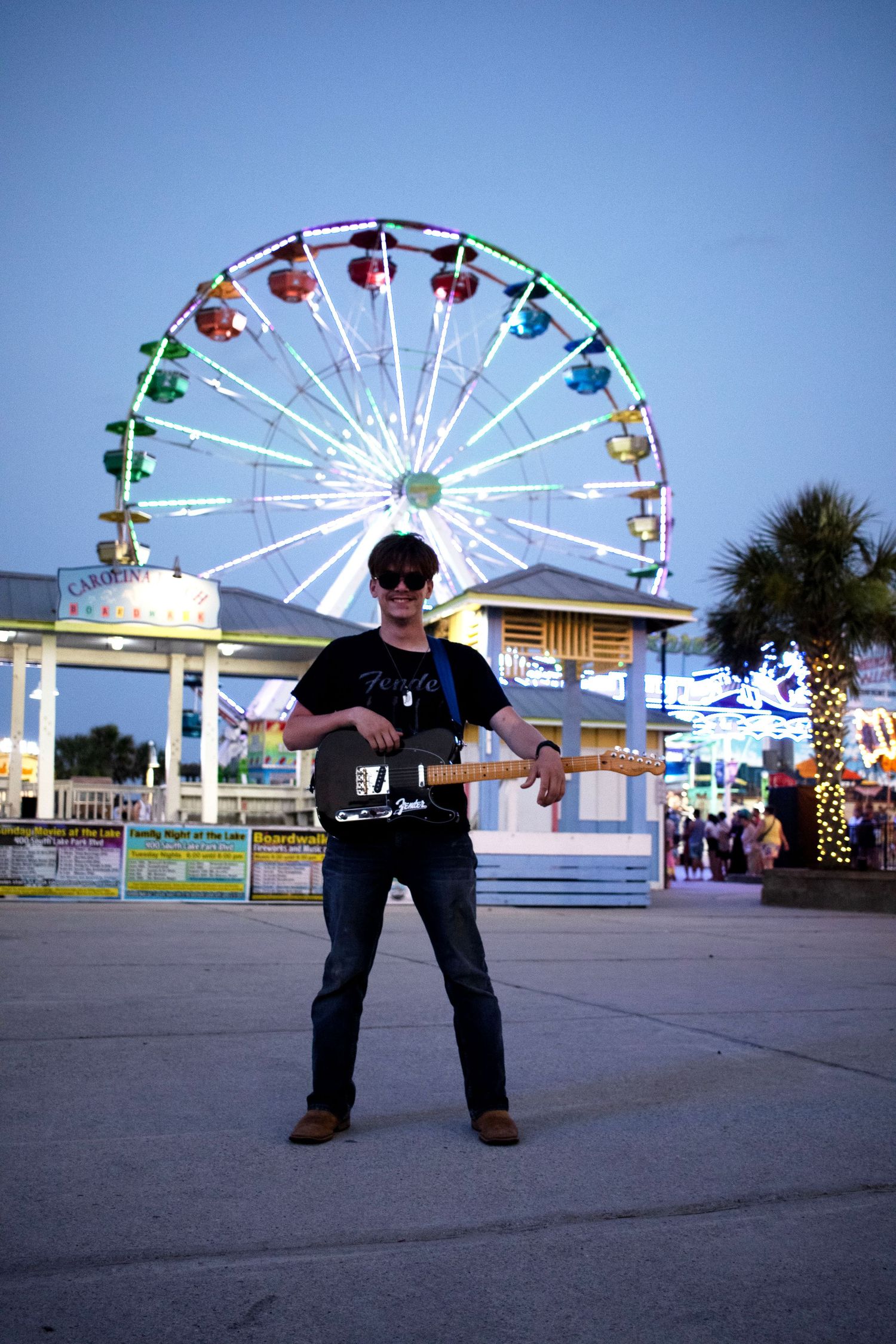 Silhouette poses against colorful ferris wheel at amusement park during dusk.