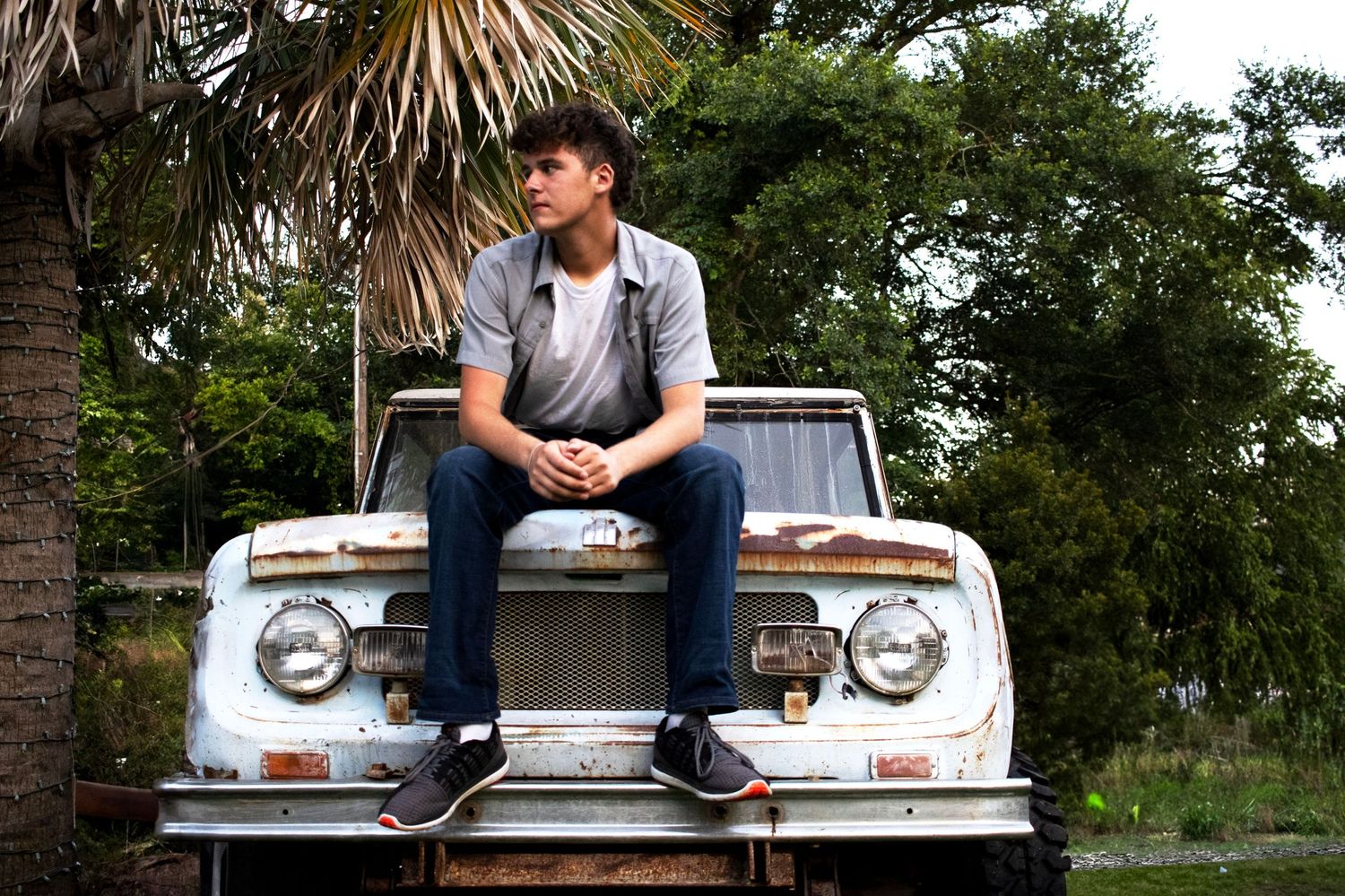 Person sitting casually on vintage truck hood under palm trees.