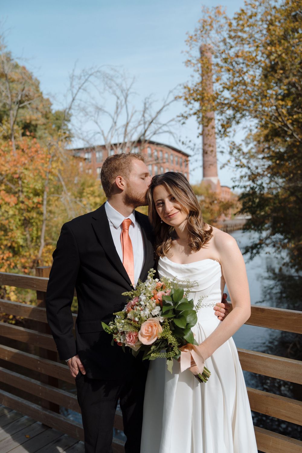 Romantic autumn wedding photos on wooden deck overlooking water with floral bouquet.