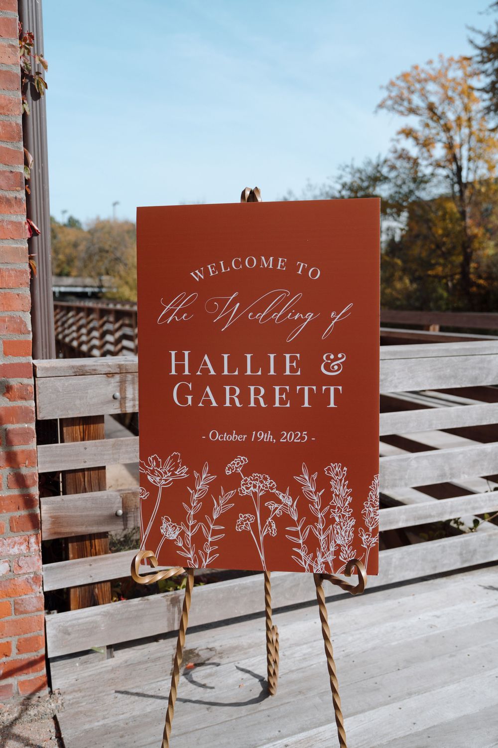Rustic terracotta wedding welcome signs displayed on wooden posts against a lattice backdrop.