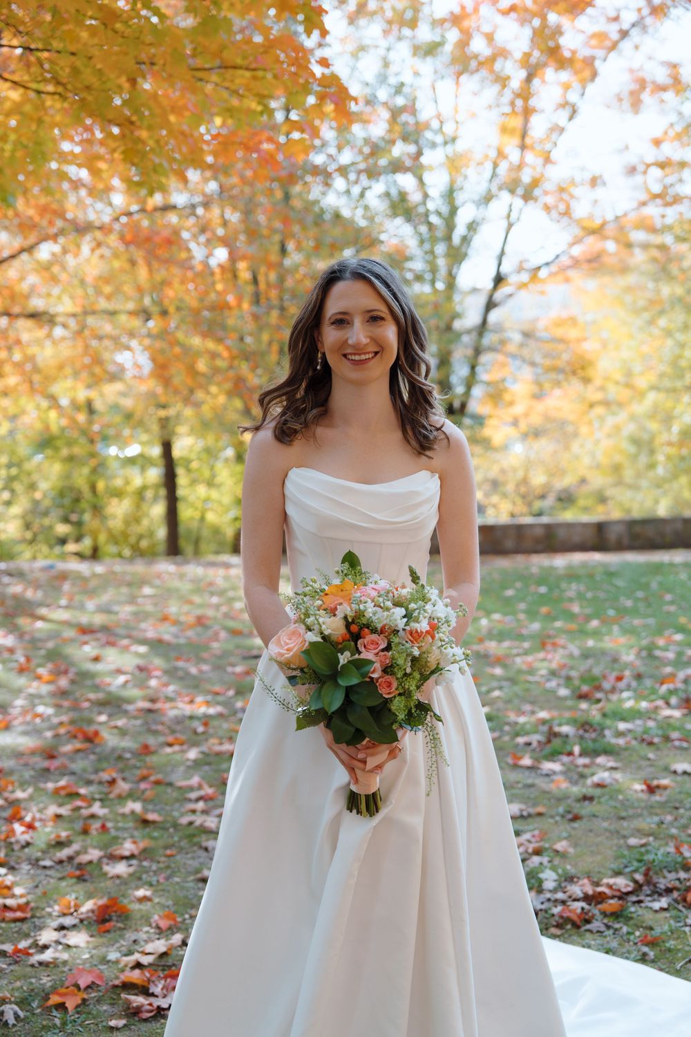Autumn wedding scene with colorful fall foliage and white dress details.