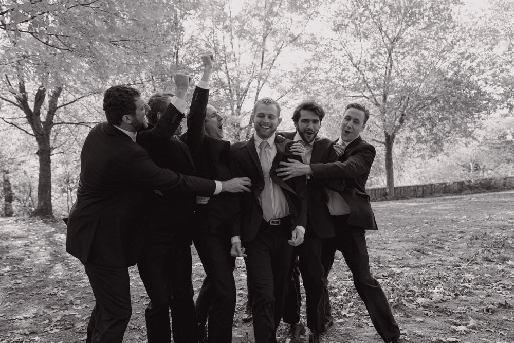 A group of people in dark clothing dance together outdoors in a black and white photograph.