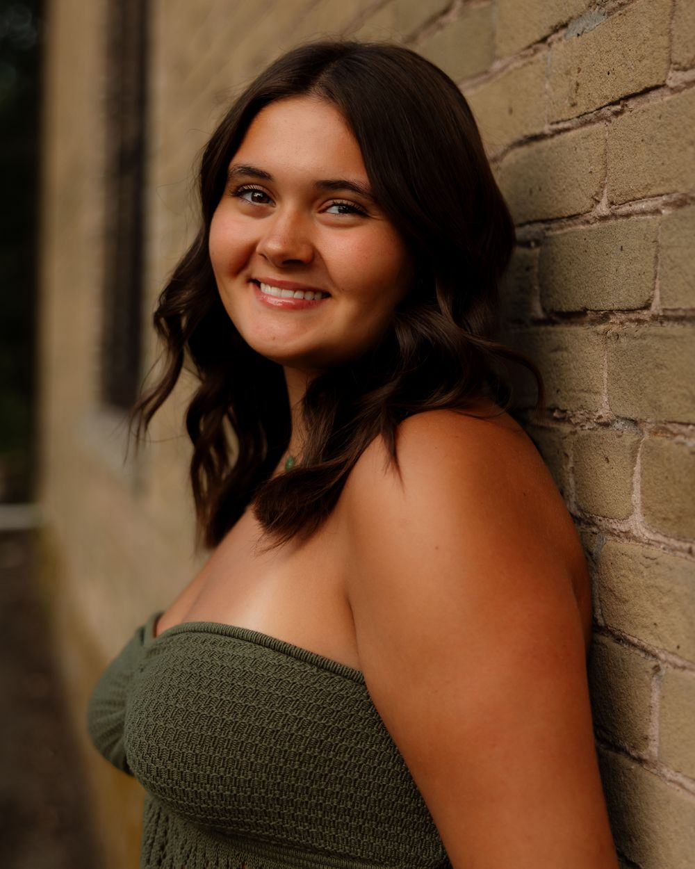 Portrait series against a brick wall featuring a dark green sweater and natural lighting at sunset.