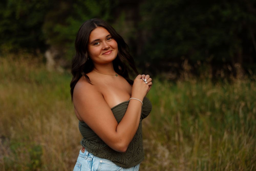 A person in a strapless dress poses outdoors in a field during golden hour lighting.