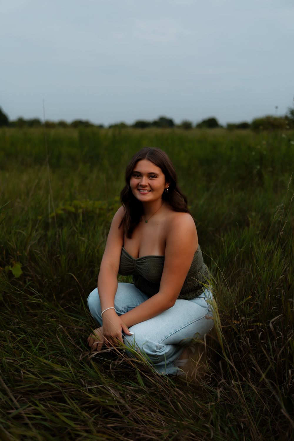 A woman in a blue dress poses gracefully in a field of tall grass during golden hour.