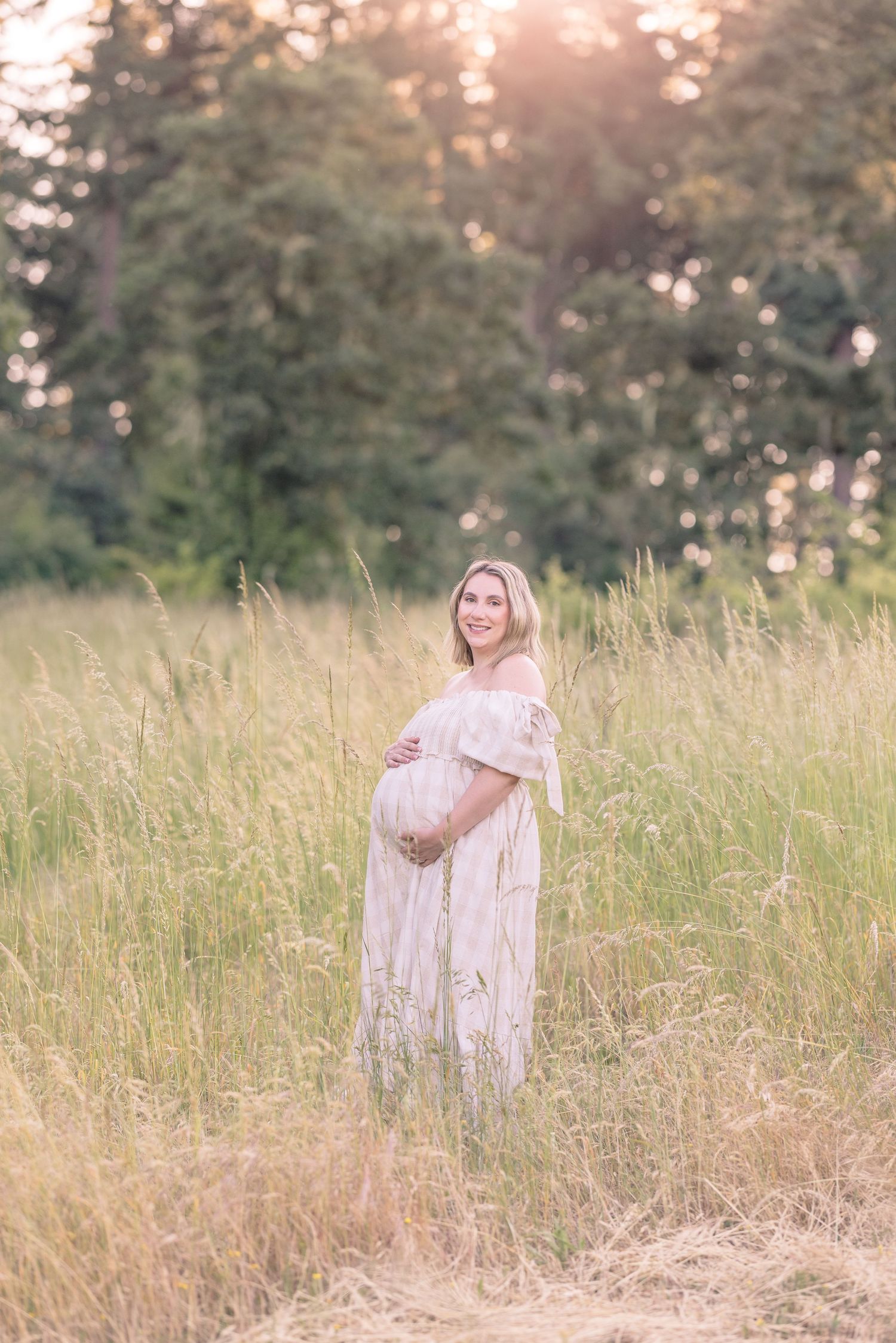 Woman in flowing dress poses in tall grass during golden hour.