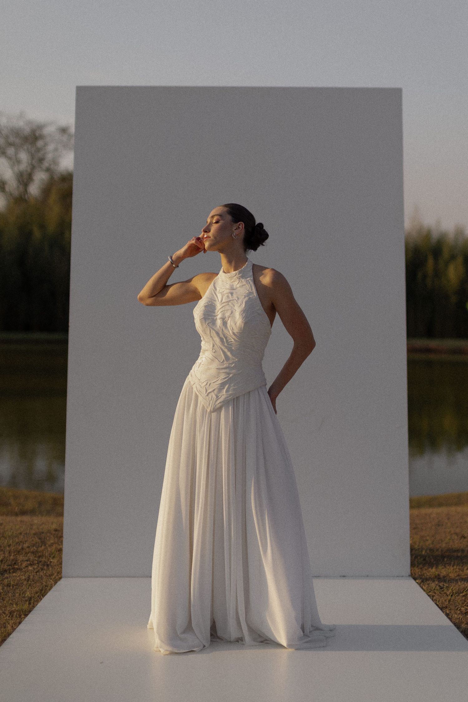 Artistic series of a bride in a flowing white dress posing against a gray backdrop outdoors.
