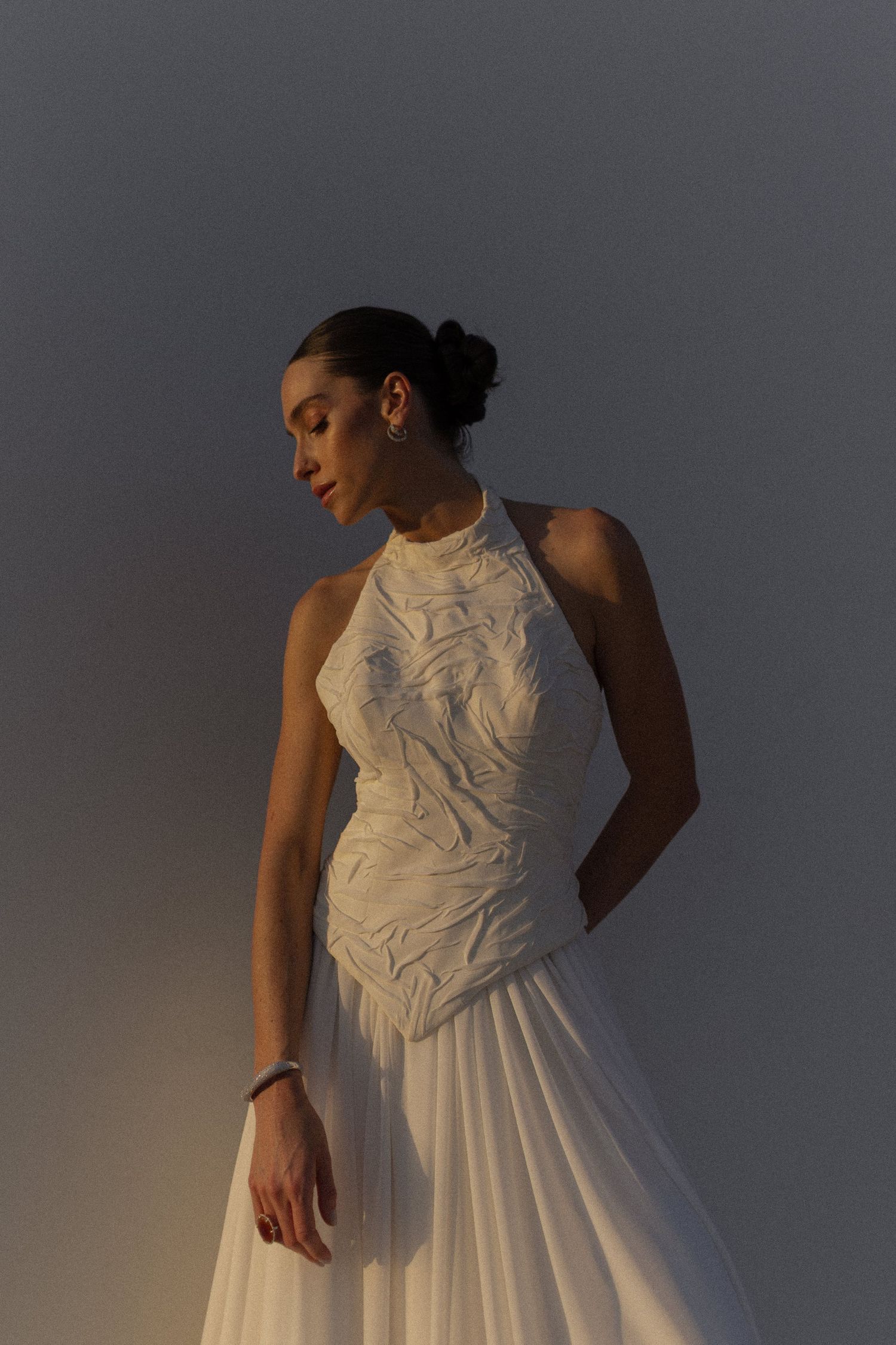 A white high-neck wedding dress with textured details captured against a grey background.