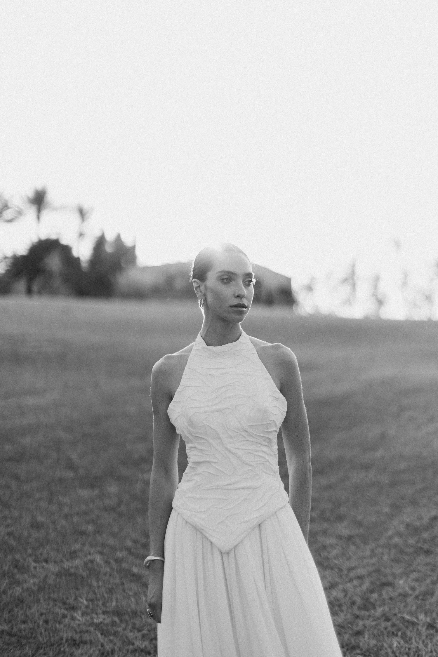 Person in white dress standing in an open grassy field at dusk.