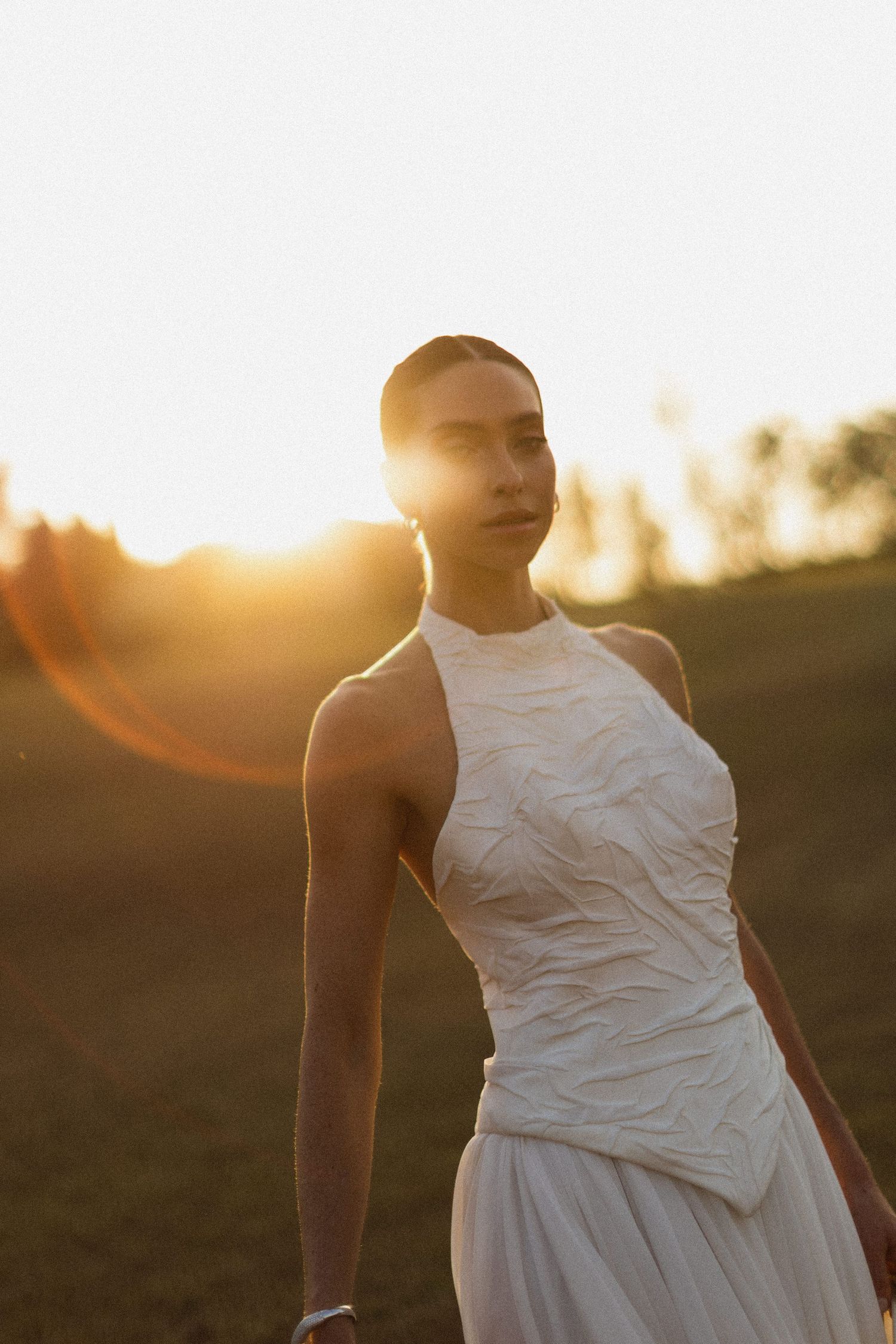 A white wedding dress silhouetted against a golden sunset in an outdoor setting.