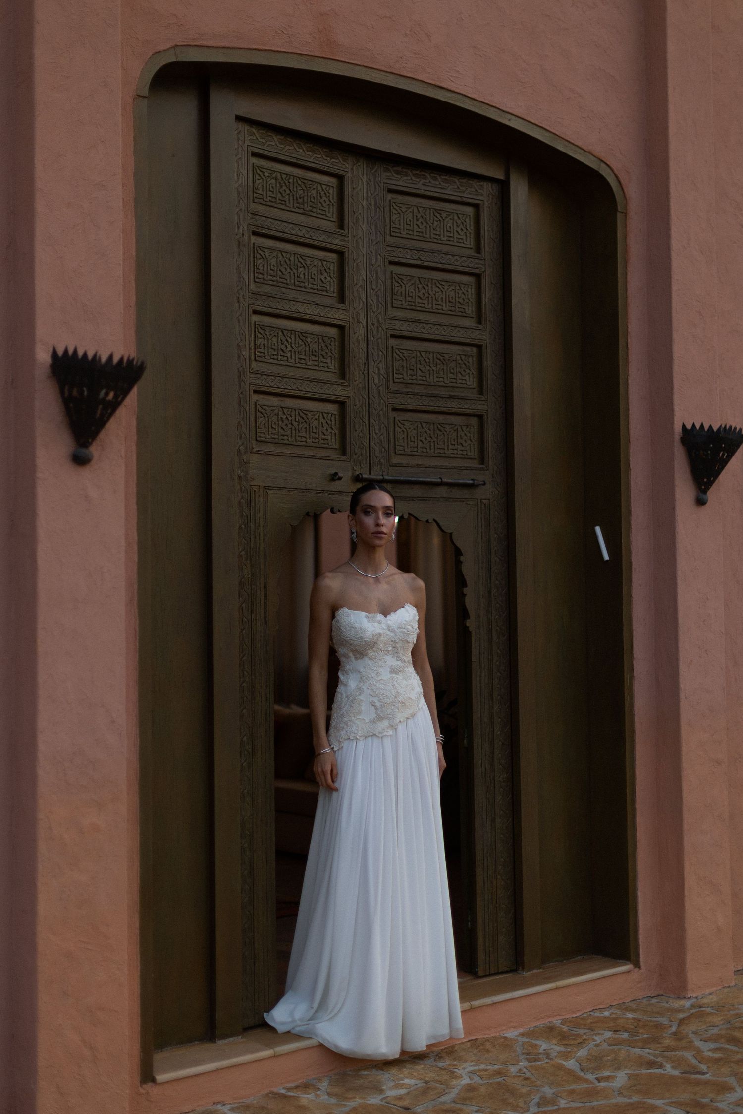 A white wedding gown photographed against terracotta walls and dark wooden doors.