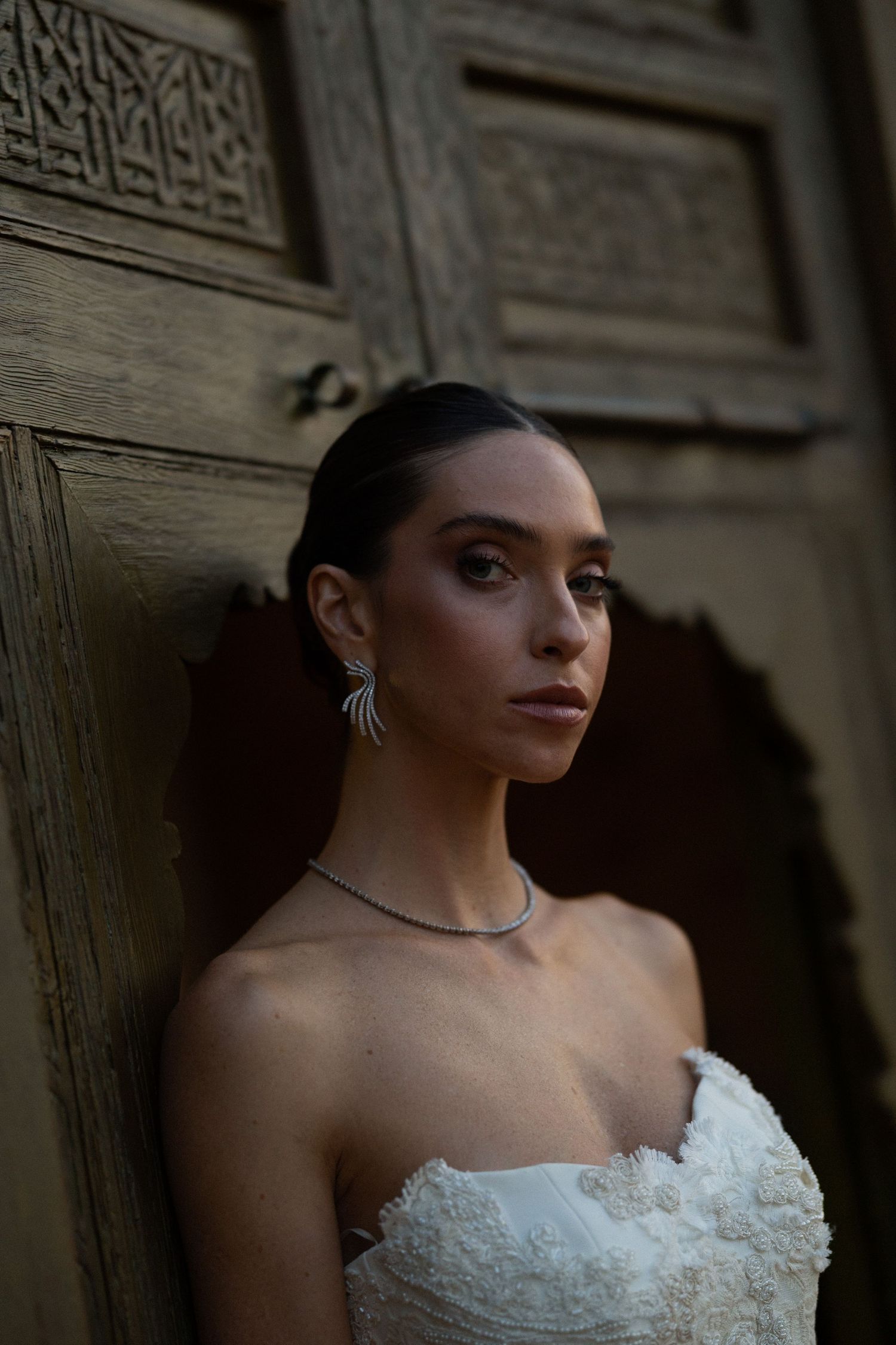 A strapless white lace wedding dress photographed against a dark textured wall.
