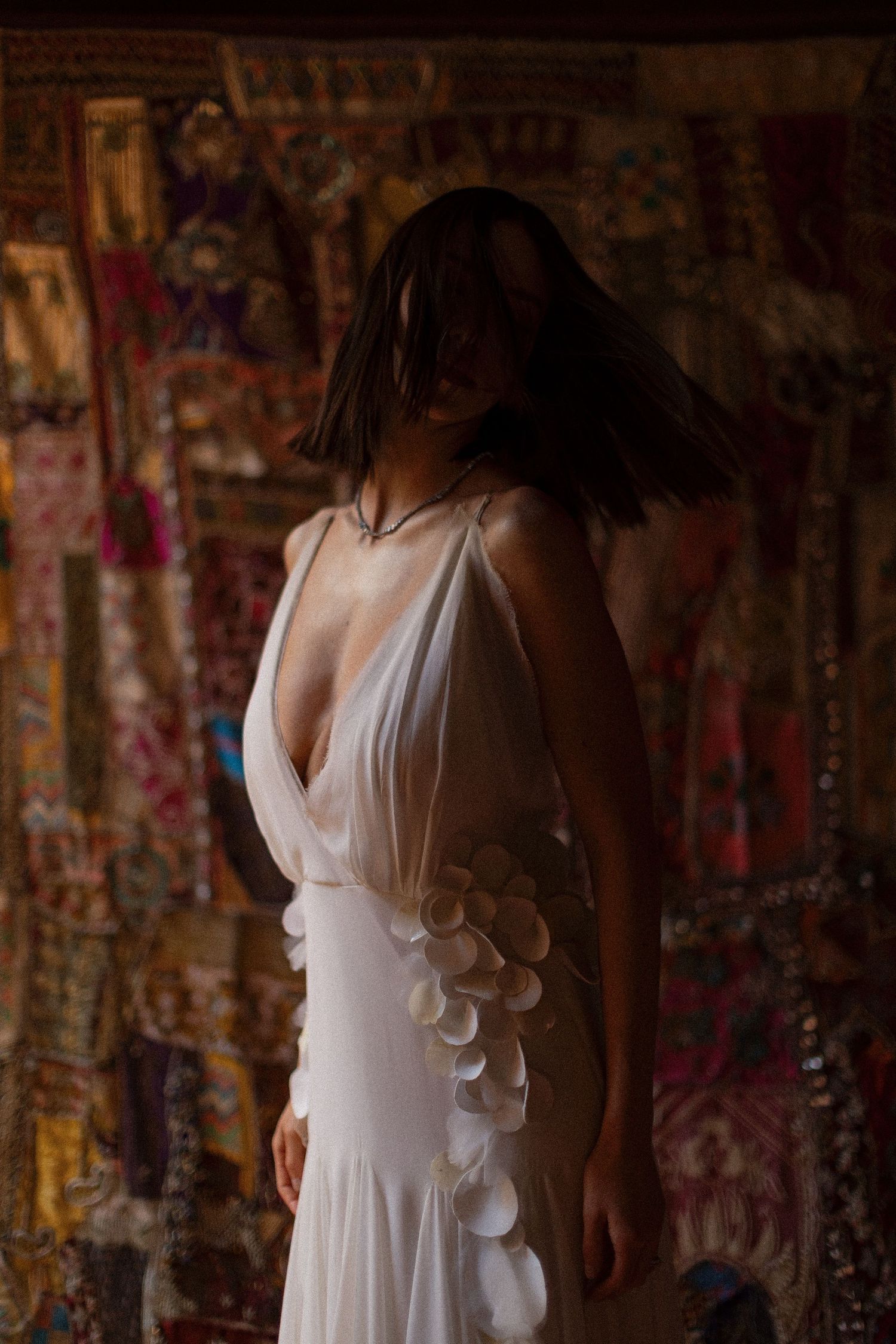 A white flowy dress with ruffled details is displayed against a textured brick wall background.