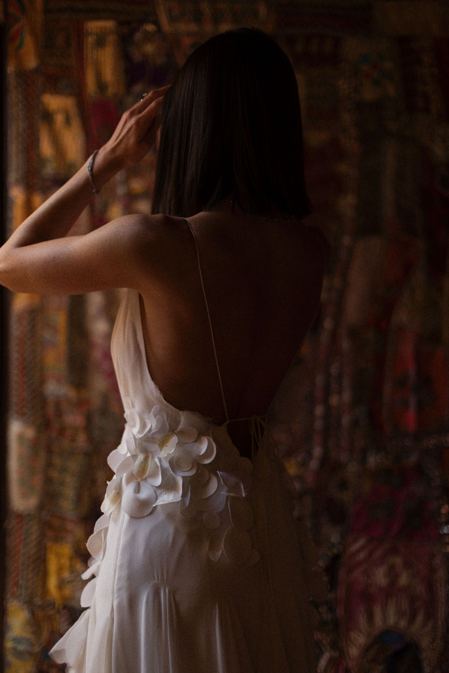 An elegant white dress with delicate ruffles hangs gracefully in front of a rustic brick wall setting.