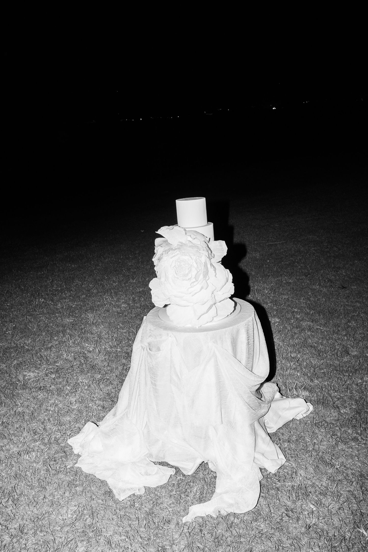 A white fabric installation or dress lies crumpled on dark ground creating dramatic shadows.