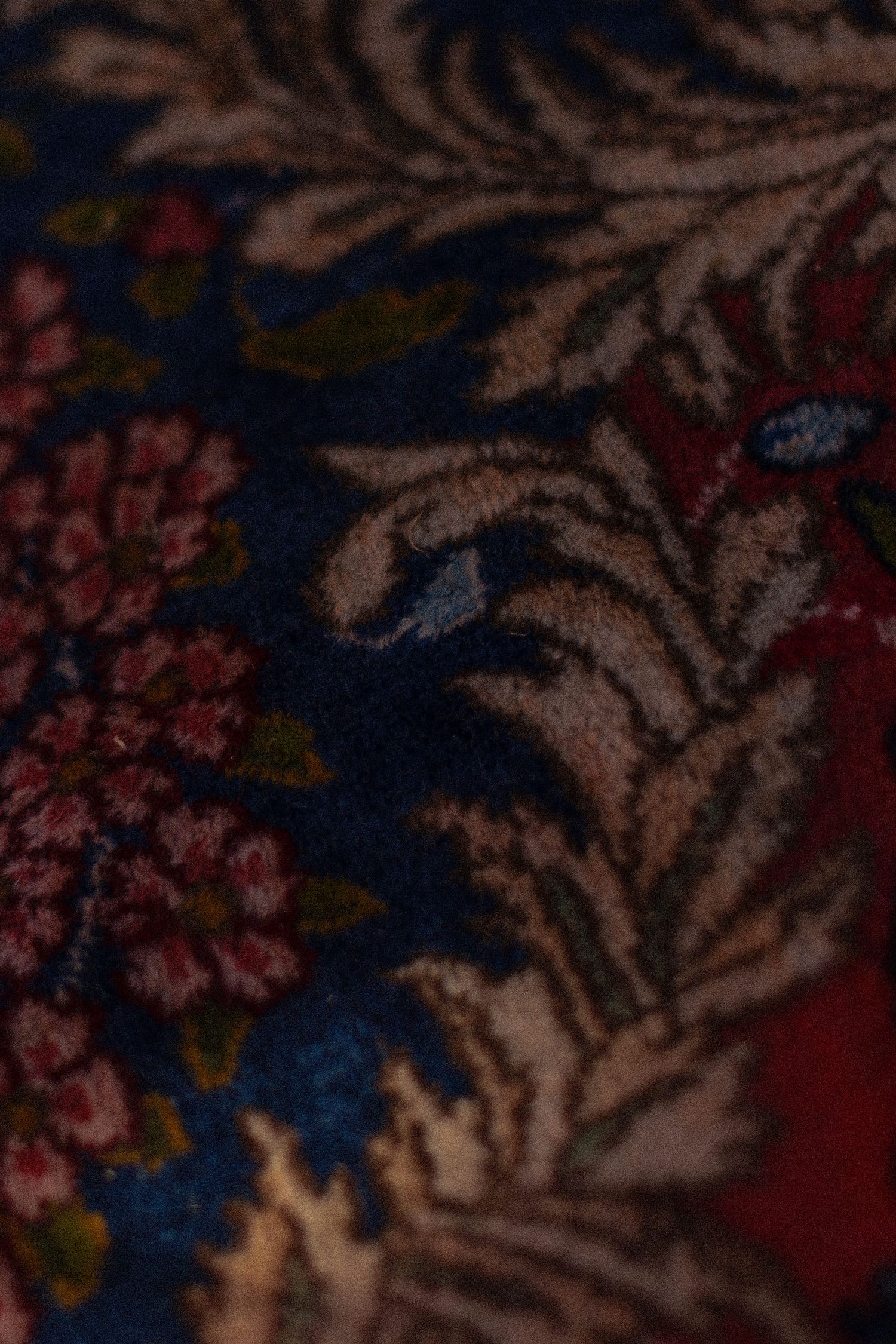 Close-up details of a floral patterned textile with pink flowers and brown leaves against a dark blue background.