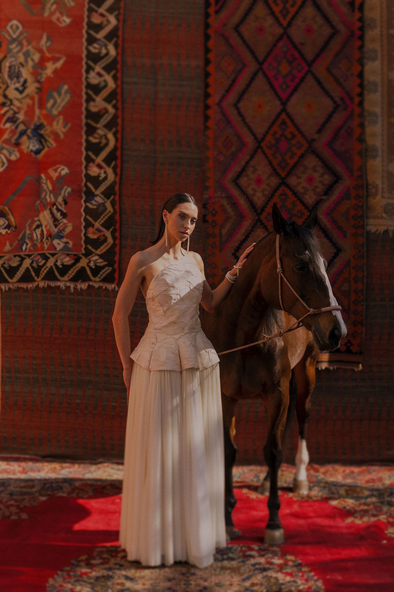 A white dress stands elegantly displayed against ornate red and brown patterned rugs.