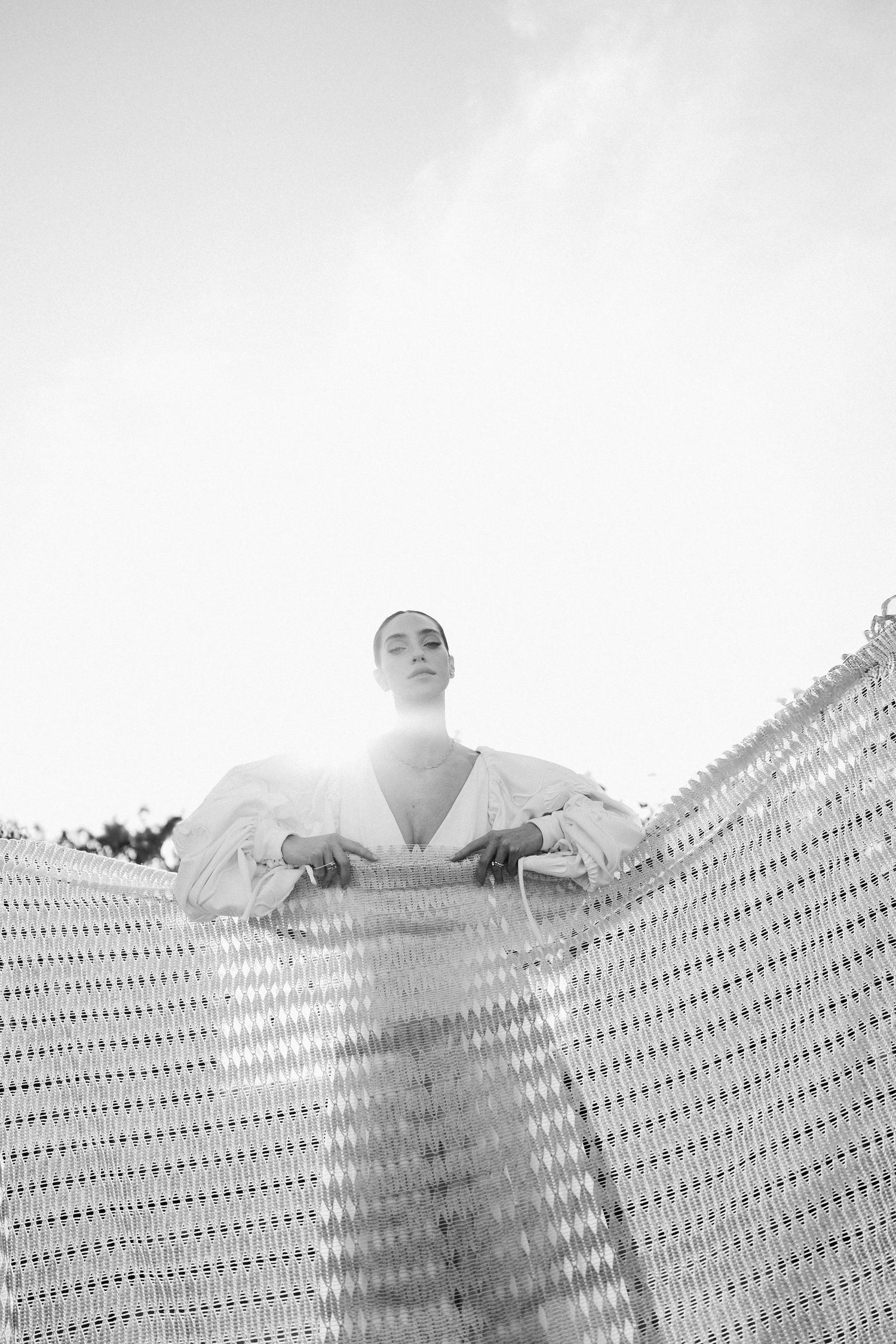 A black and white artistic photo showing a figure peeking over a mesh fence or screen pattern.