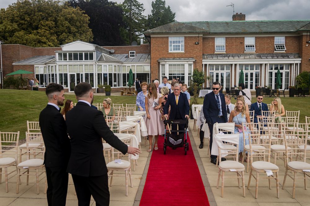 Wedding ceremony setup with red carpet aisle and white chairs leading to an outdoor pavilion.
