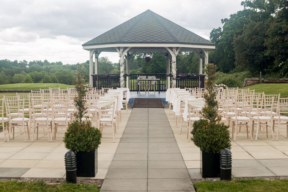 White chairs arranged in rows leading to a covered pavilion for an outdoor wedding ceremony.
