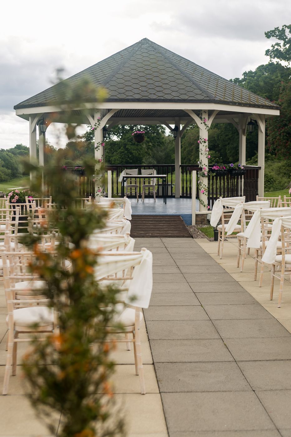 Outdoor wedding venue setup with white chairs and a gazebo under cloudy skies.