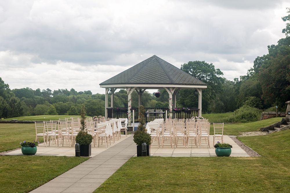 Panoramic view of an outdoor wedding venue with white chairs leading to a gazebo.