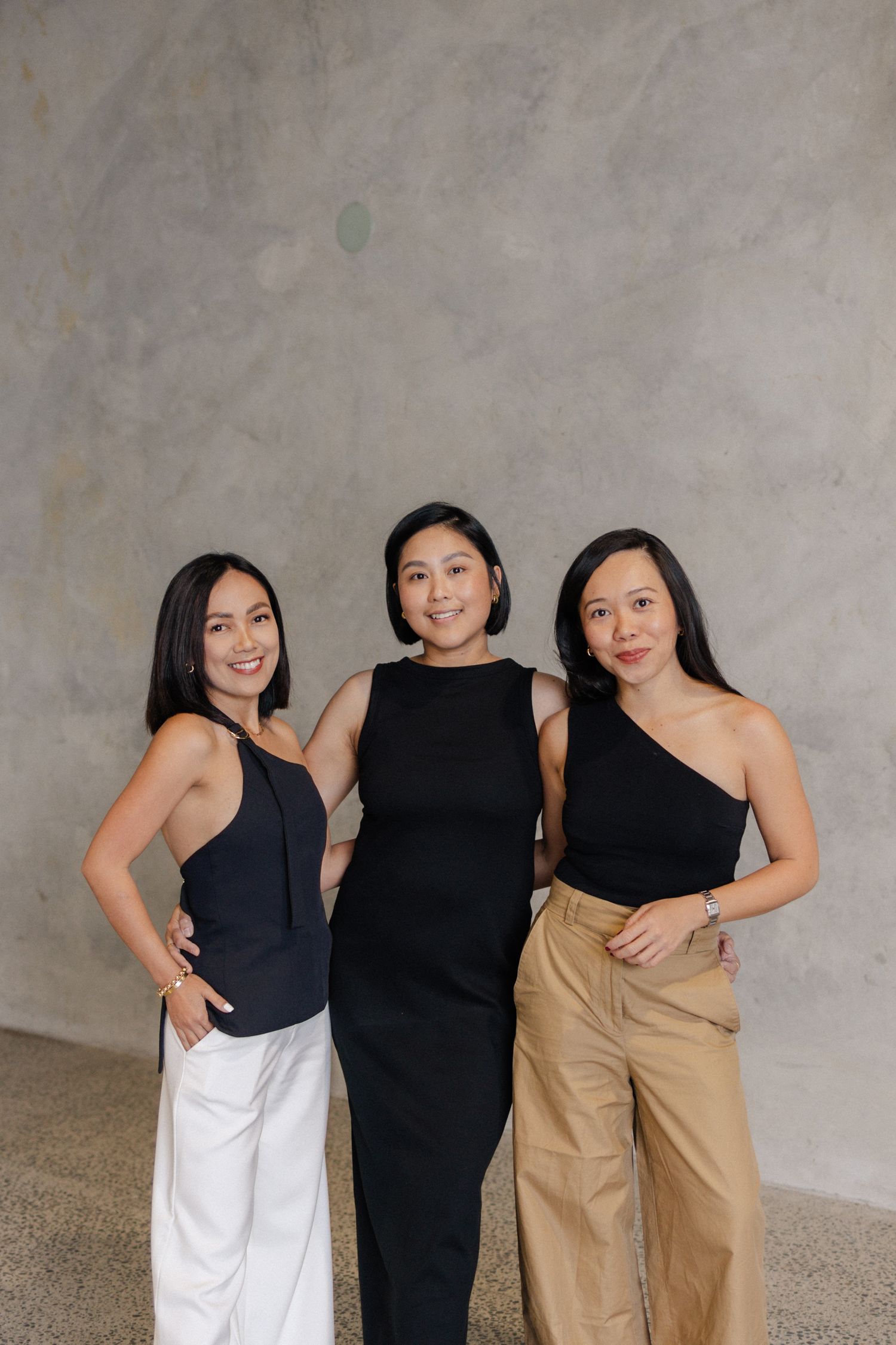 Group portrait of women in coordinated neutral outfits against textured grey wall.