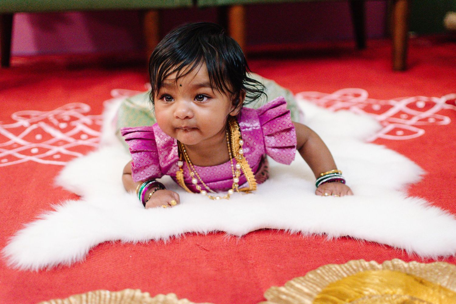 Baby laying on red mat surrounded by symbolic ritual items during Annaprashana ceremony.
