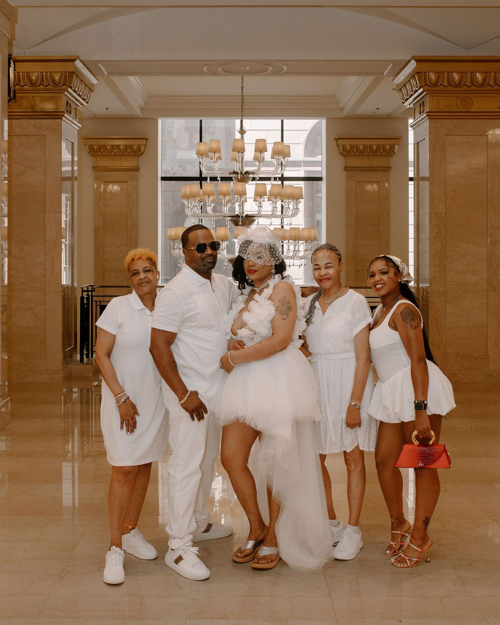 Group in all-white outfits poses together in a grand ballroom with decorative architectural details.