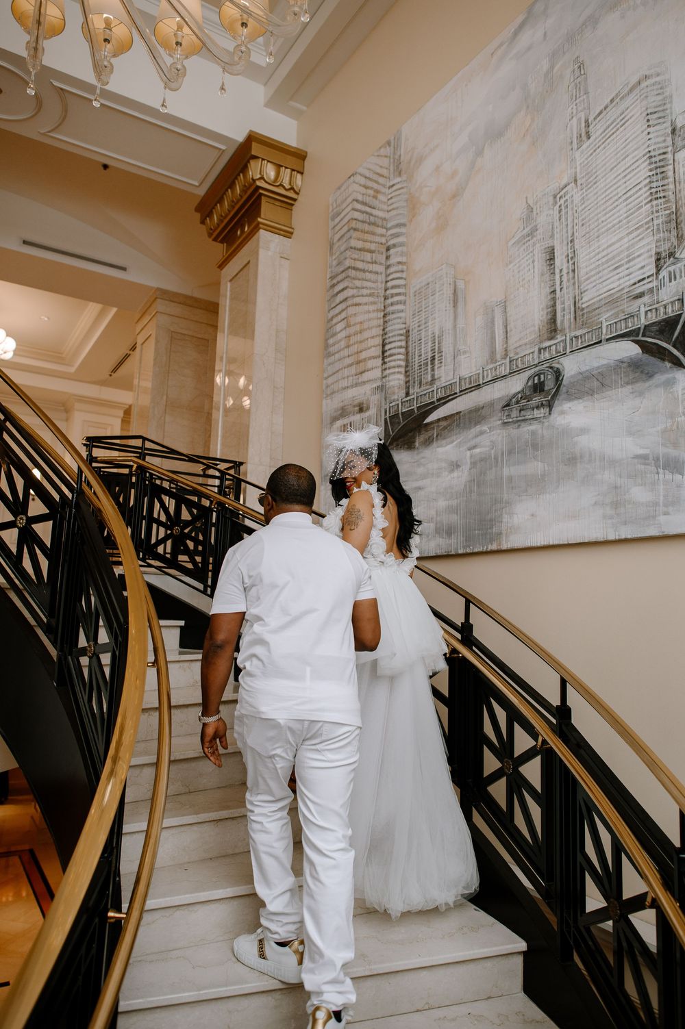 Romantic couple ascending grand staircase with black railings and urban artwork on walls.
