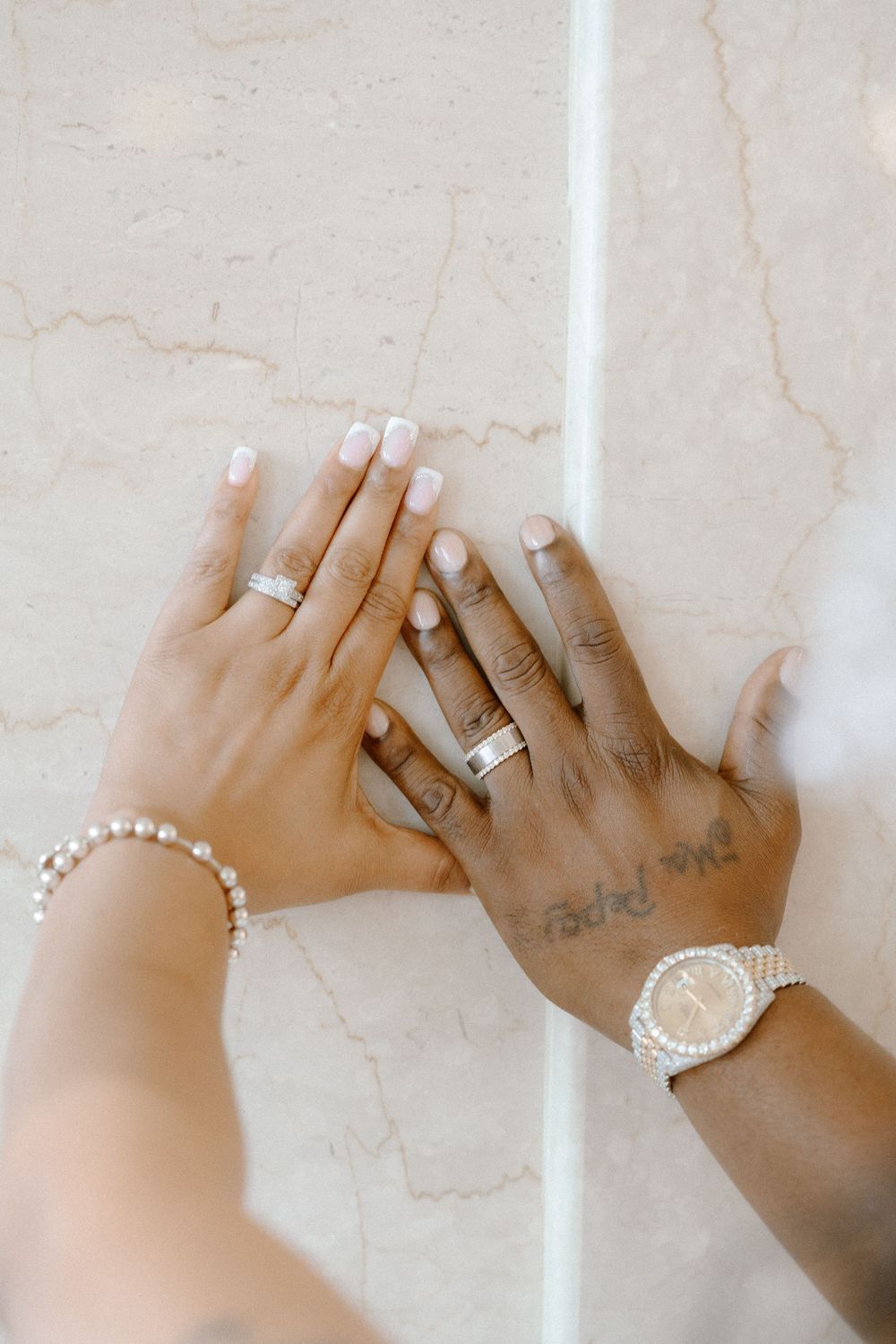 Two hands wearing pearl bracelets and rings reach across a marble surface in a sequence of photos.