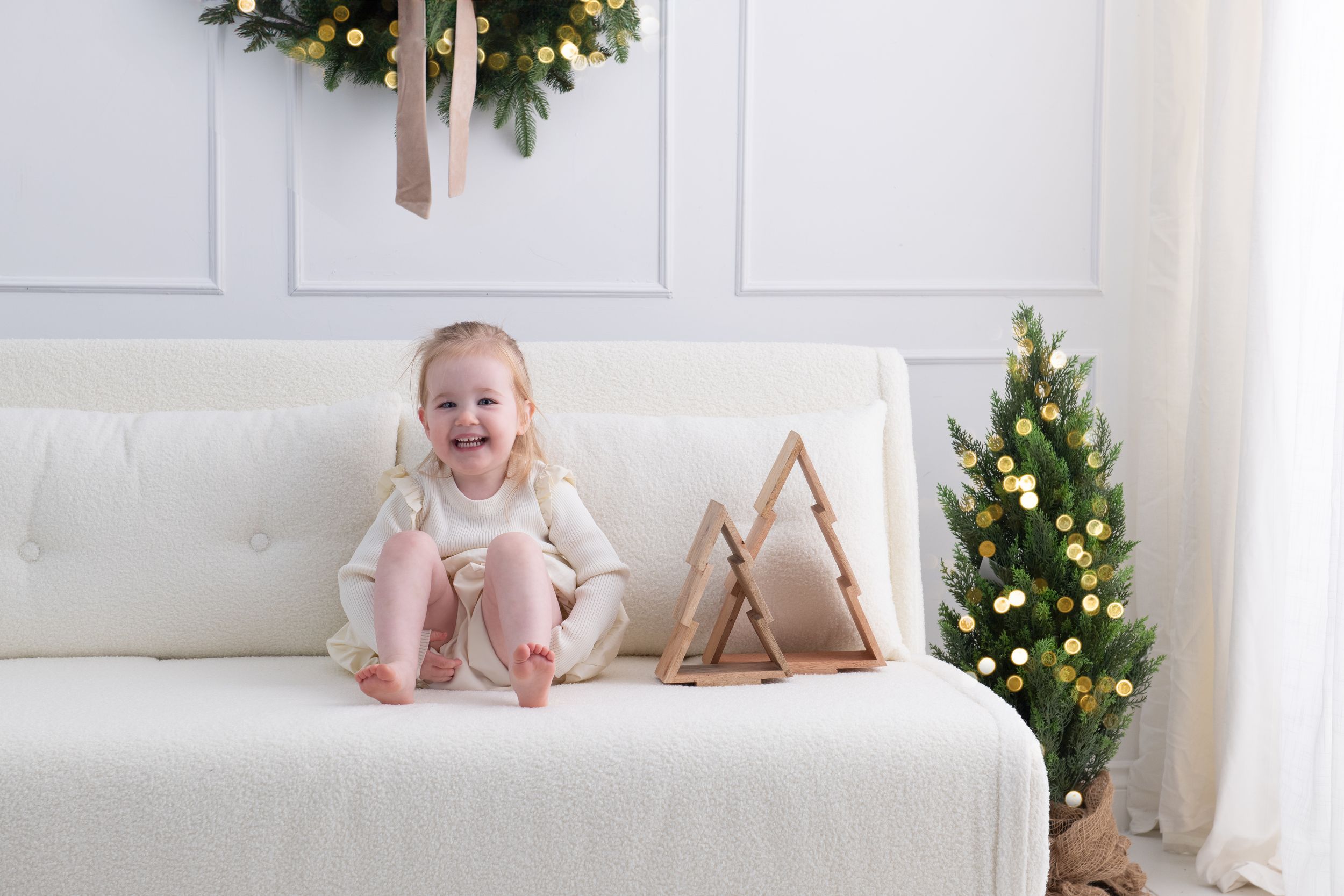 Cozy Christmas scene with decorated trees, white furniture, and soft neutral decor in a bright modern interior.