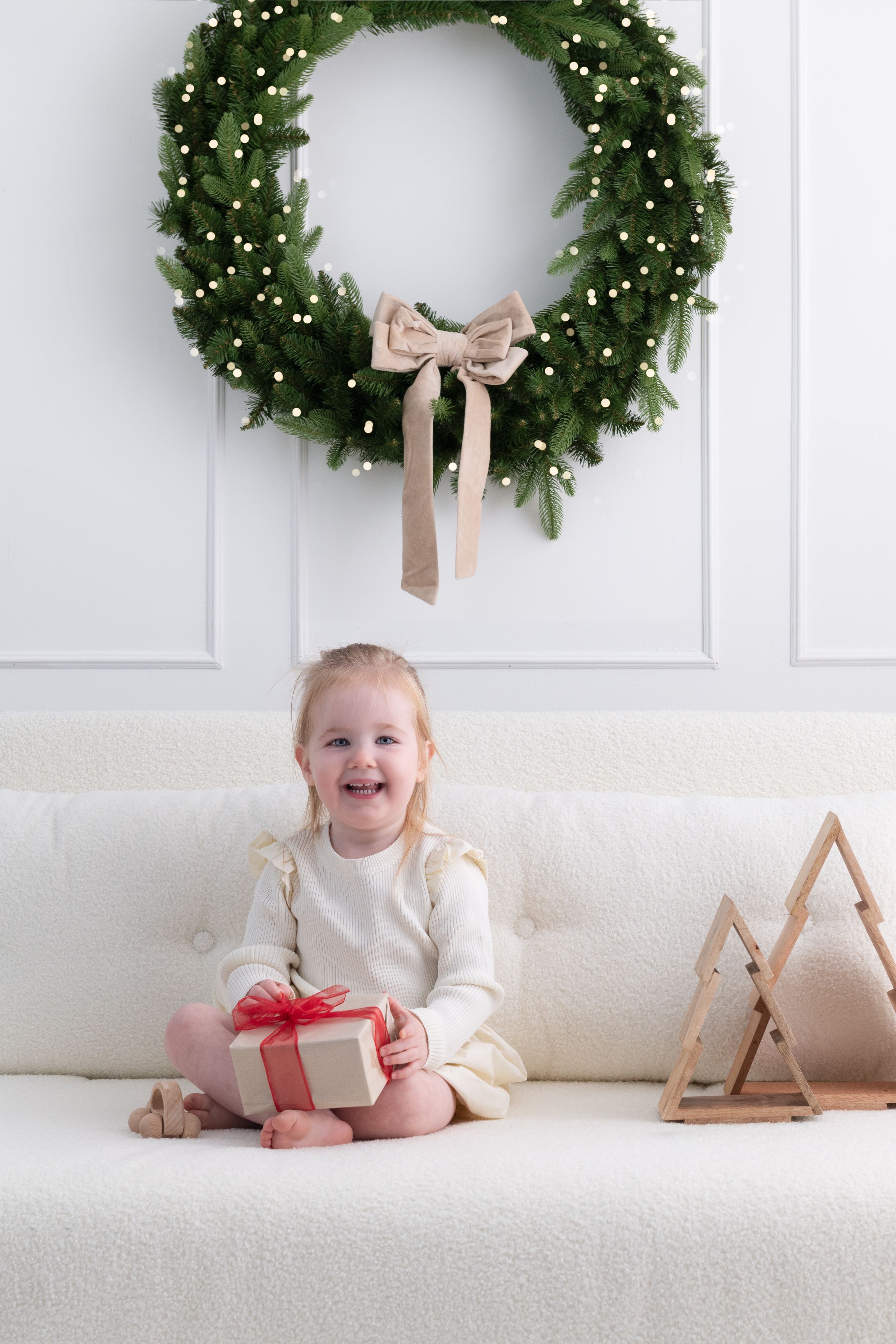 A festive holiday scene with evergreen wreaths on white walls and cozy decor on a light colored couch.