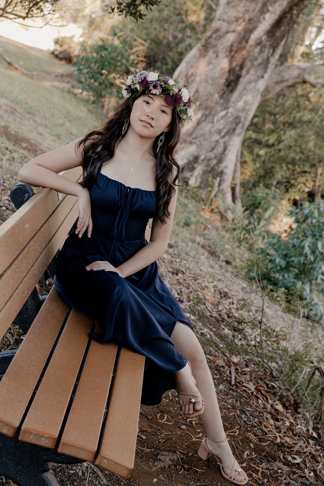 A person in a navy blue dress reclines on a wooden bench in an outdoor garden setting.