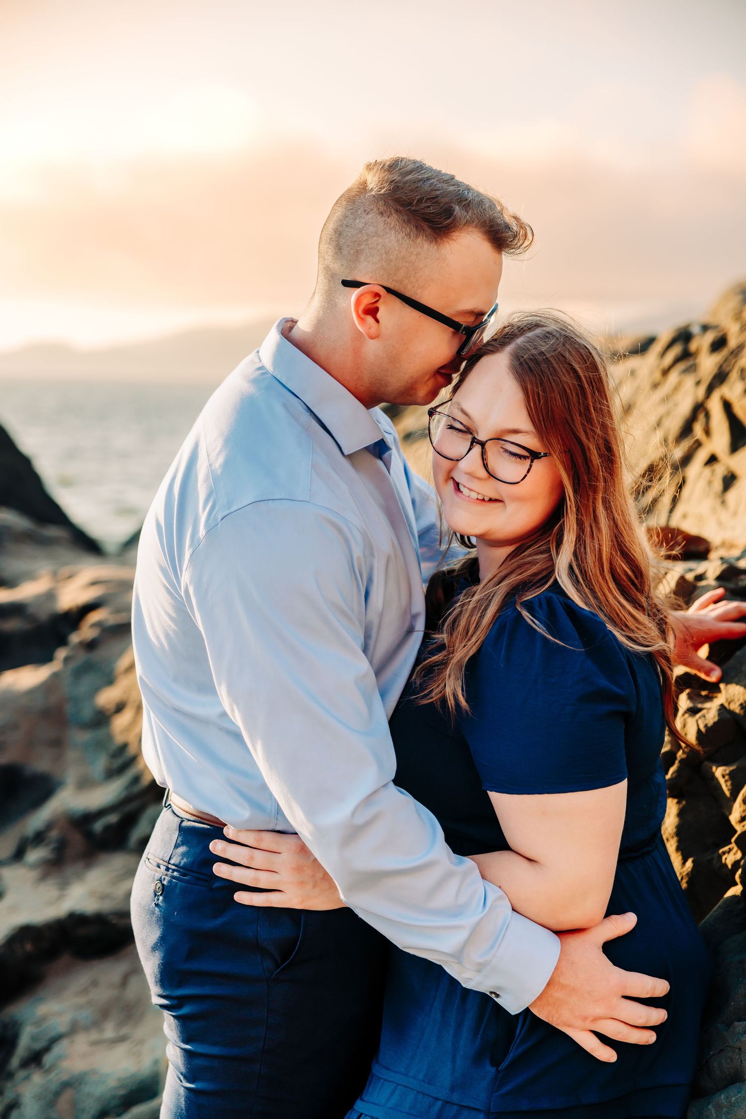 A couple embraces during a romantic sunset photoshoot along rocky coastal cliffs.