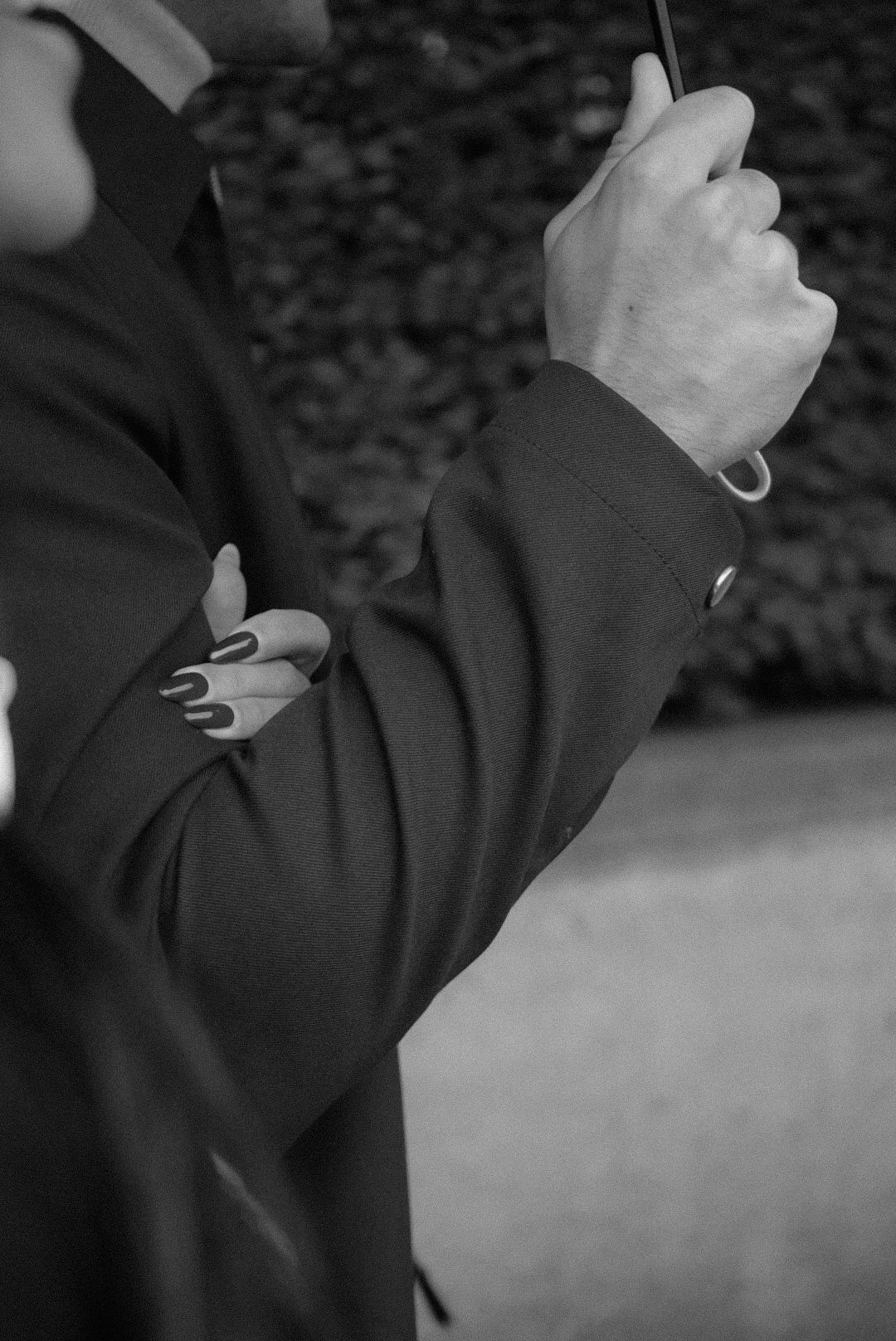 Black and white detail shot of hands with painted nails against dark background.